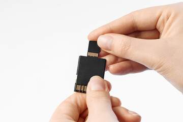 Inserts micro sd into sd card reader, female hands, closeup. On white background.