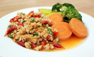 Close up Minced pork spicy salad in white plate eat with chili, carrot, pumpkin and broccoli, isolated in wooden table blur background, famous traditional food of Thailand. Thai style food restaurant.