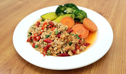 Minced pork spicy salad in white plate eat with chili, carrot, pumpkin, broccoli and vegetables, isolated in wooden table background, famous traditional food of Thailand. Thai style food restaurant.