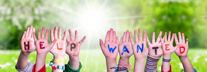 Children Hands Building Colorful English Word Help Wanted. Sunny Green Grass Meadow As Background