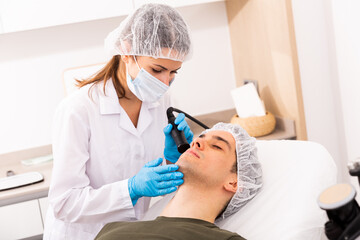 Female beautician performing face needle-free mesotherapy for male