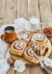 Basket of homemade buns with jam, served on old wooden table with walnuts and cup of milk