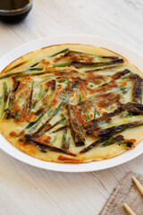Homemade korean Pajeon scallion pancake on a white plate on a white wooden surface, low angle view. Asian food. Close-up.