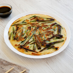 Homemade korean Pajeon scallion pancake on a white plate on a white wooden background, side view. Asian food.