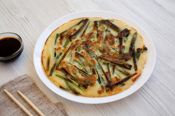 Homemade korean Pajeon scallion pancake on a white plate on a white wooden surface, side view. Asian food.
