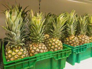 Pineapple fruits in a green box on a shelf in store. Grocery section in supermarket. Fruit trade concept.