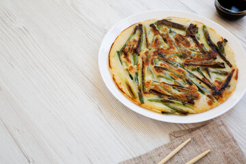 Homemade korean Pajeon scallion pancake on a white plate on a white wooden background, side view. Asian food. Copy space.