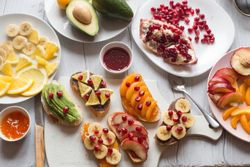 Process of making sweet toast with jam and various fruits apricots, peaches, bananas, oranges and avocado decorated with pomegranates on top.