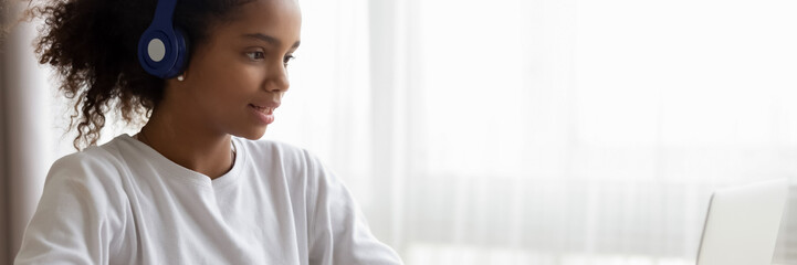 African teenage girl wear headphones use laptop learning language on-line, do school subject tasks...