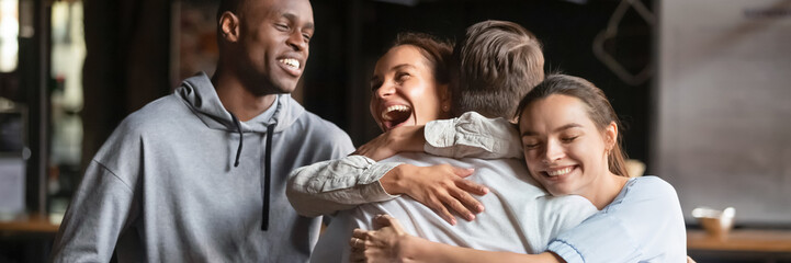 Gathered in cafe diverse friends meet guy mate cuddle him feel happy young people glad to see each...