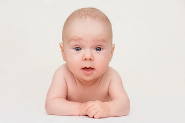 The newborn baby lies on the tummy on a white background and looks into the camera. 