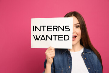 Emotional woman holding paper with text INTERNS WANTED on pink background