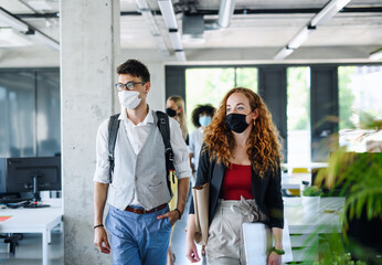 Young people with face masks back at work in office after lockdown, walking.