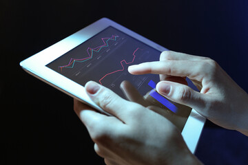Broker using tablet on dark background, closeup. Forex trading
