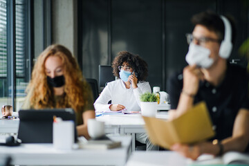 Young people with face masks back at work or school in office after lockdown.