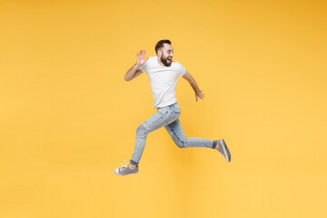 Fototapeta na wymiar Side view of cheerful young bearded man guy in white casual t-shirt posing isolated on yellow background. People lifestyle concept. Mock up copy space. Jump like running looking aside spreading hands.