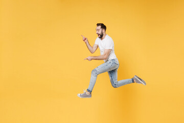 Fototapeta na wymiar Side view of excited young bearded man guy in white casual t-shirt posing isolated on yellow wall background studio. People lifestyle concept. Mock up copy space. Jumping pointing index fingers aside.