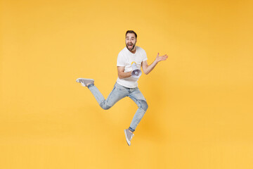 Fototapeta na wymiar Surprised young bearded man guy in white casual t-shirt posing isolated on yellow background studio portrait. People lifestyle concept. Mock up copy space. Jumping, hold megaphone, spreading hands.