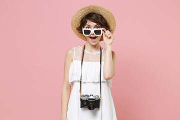 Excited young tourist woman in summer dress hat sunglasses with photo camera isolated on pink...