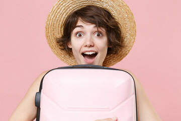 Excited young tourist girl in hat isolated on pink wall background studio portrait. Female traveling abroad to travel weekend getaway. Air flight journey concept. Hold suitcase keeping mouth open.