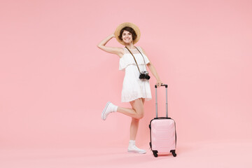 Smiling young tourist girl in summer dress hat with photo camera suitcase isolated on pink background. Female traveling abroad to travel weekend getaway. Air flight journey concept. Put hand on head.