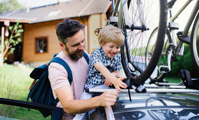 Father with small son putting bicycles on car roof, going on trip concept.
