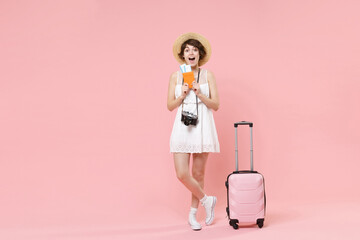 Excited tourist girl in dress hat with suitcase photo camera isolated on pink background. Traveling abroad to travel weekends getaway. Air flight journey concept. Hold passport tickets boarding pass.
