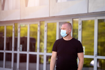 Portrait of brunette man in a medical surgical mask in the city.