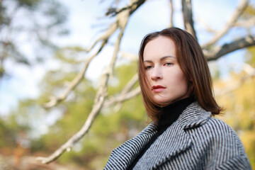 Beautiful caucasian woman in gray coat siting on the tree in the forest in autumn season 