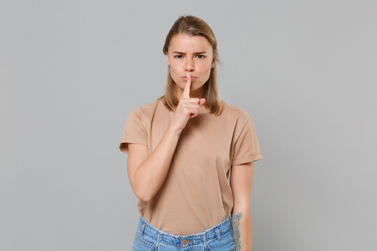 Secret young blonde woman girl in casual beige t-shirt posing isolated on gray background studio. People lifestyle concept. Mock up copy space. Saying hush be quiet with finger on lips shhh gesture.