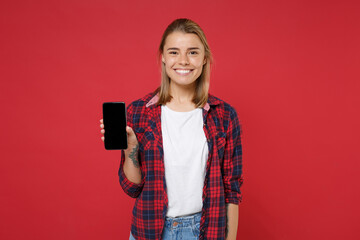 Smiling young blonde woman girl in casual checkered shirt posing isolated on red background studio portrait. People lifestyle concept. Mock up copy space. Hold mobile phone with blank empty screen.