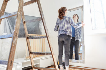 Junge Frau hängt einen Spiegel an die Wand