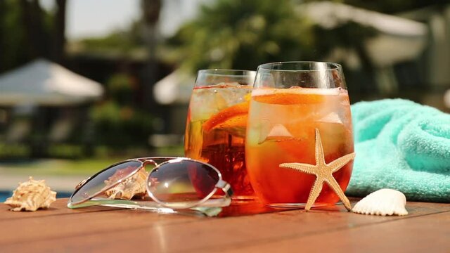 Glasses of aperol spritz or negroni cocktail with seashells, towel and sunglasses at the summer patio. Vacation, summer, holiday, luxury resort concept