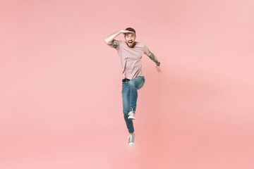 Fototapeta na wymiar Excited young bearded tattooed man guy in pastel casual t-shirt isolated on pink background. People lifestyle concept. Mock up copy space. Jumping, holding hand at forehead looking far away distance.
