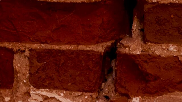 A long crack in the old masonry. A wall of red brick and white lime mortar. The remains of crumbling plaster. Warm daylight. 4K.