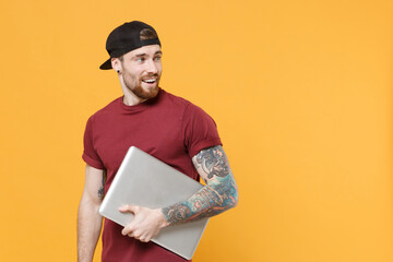 Amazed young bearded tattooed man guy in casual t-shirt black cap posing isolated on yellow...