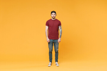 Fototapeta premium Handsome young tattooed man guy in casual t-shirt black cap posing isolated on yellow wall background studio portrait. People sincere emotions lifestyle concept. Mock up copy space. Looking camera.