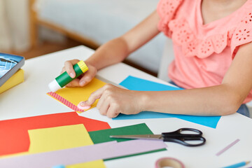 childhood, creativity and hobby concept - close up of creative girl making greeting card and sticking paper stripe with glue stick at home
