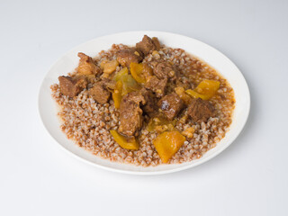 Hungarian goulash. Buckwheat with beef. White round plate on a white background