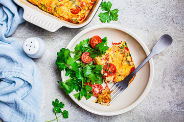 Classical baked frittata or omelet with tomatoes, peppers and cheese in white plate, light gray background.