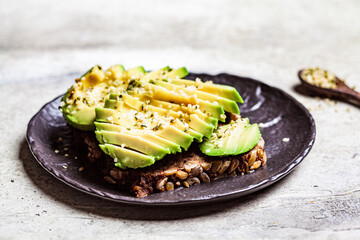 Avocado toast with rye bread and hemp seeds on black plate. Healthy vegan food concept.