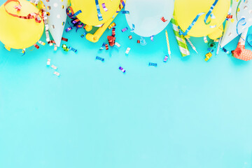 Birthday balloon background with colorful party streamers, confetti and birthday party hats on blue bacground top view