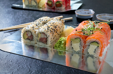 Set of sushi rolls, sauce, wasabi and hand with chopsticks on dark background. Sushi restaurant menu. Various kinds of sushi. Japanese food. Selective focus