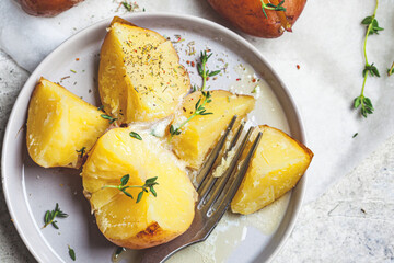 Baked potatoes with butter and thyme on gray plate, top view.