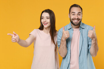 Smiling young couple two friends guy girl in pastel blue casual clothes posing isolated on yellow background. People lifestyle concept. Mock up copy space. Point index finger aside, showing thumbs up.