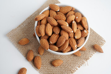 almonds in white bowl and glass of milk and brown fabric on white background. top view and flat lay, 