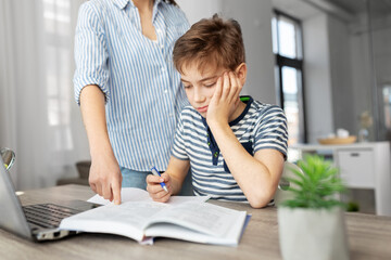 education, family and homework concept - mother and son with book writing to notebook at home