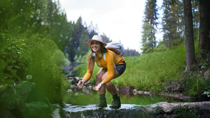 Happy young woman standing by stream on a walk outdoors in summer nature.