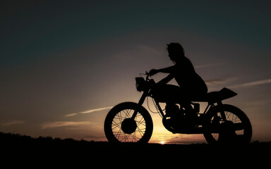 Fototapeta na wymiar Shadow of a biker girl on a sunset background, silhouette of a girl on a bike. Black motorcycle and a woman on it.