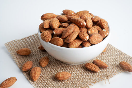 almonds in white bowl and glass of milk and brown fabric on white background. top view and flat lay, "badam"